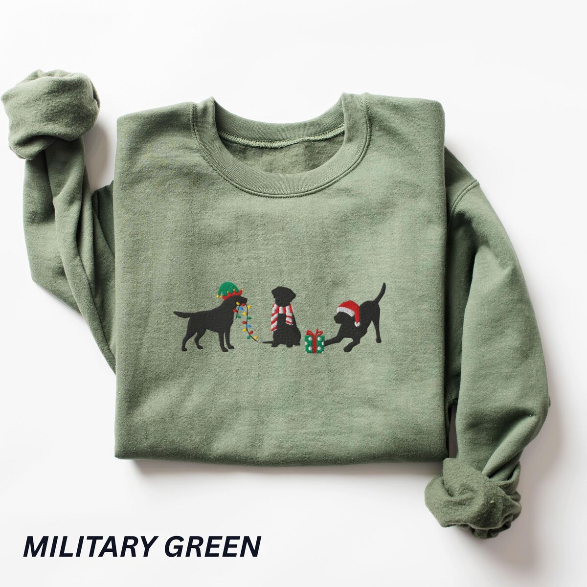 Black Lab Elf Christmas Sweatshirt - Military Green Military Green crewneck sweatshirt laid flat with a rolled cuff, embroidered with three black Labradors, one in an elf hat carrying Christmas lights, one in a candy-cane scarf and one in a Santa hat pawing a gift