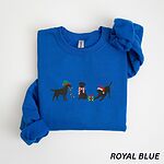 Royal crewneck sweatshirt laid flat with a rolled cuff, embroidered with three black Labradors, one in an elf hat carrying Christmas lights, one in a candy-cane scarf and one in a Santa hat pawing a gift
