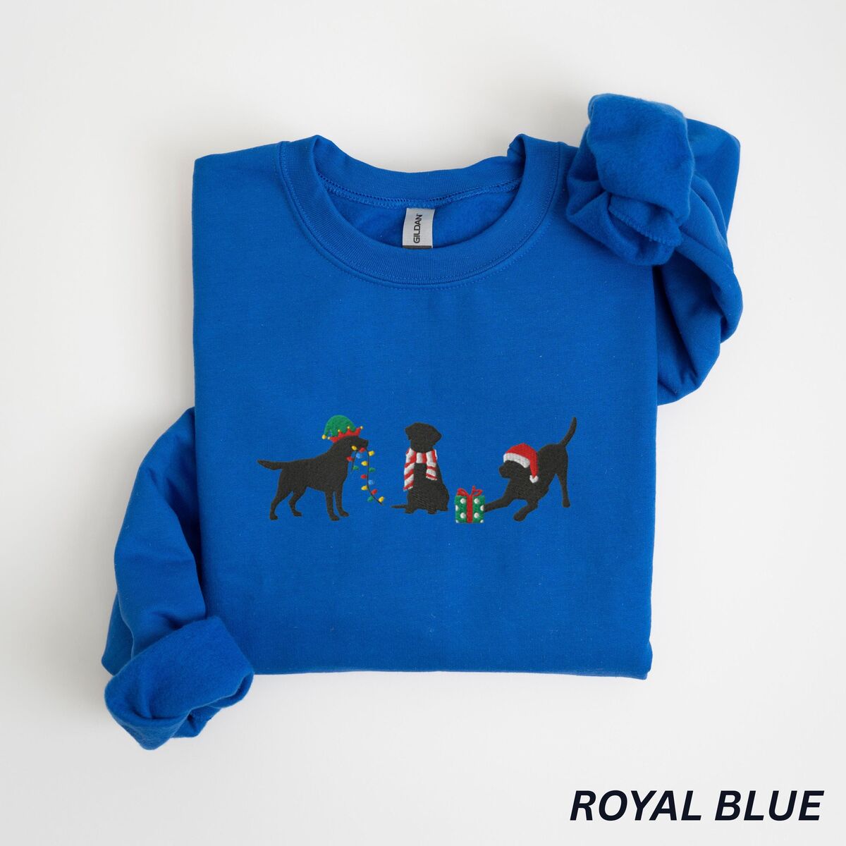 Black Lab Elf Christmas Sweatshirt - Royal Royal crewneck sweatshirt laid flat with a rolled cuff, embroidered with three black Labradors, one in an elf hat carrying Christmas lights, one in a candy-cane scarf and one in a Santa hat pawing a gift