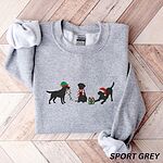 Sport Grey crewneck sweatshirt laid flat on a chevron wood floor, embroidered with three black Labradors, one in an elf hat carrying Christmas lights, one in a candy-cane scarf and one in a Santa hat pawing a gift