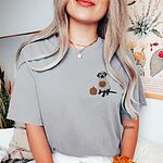 Woman in a light grey T-shirt embroidered with a small black lab in a ghost costume and a pumpkin on the left chest