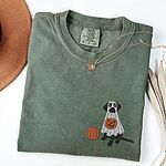 Moss T-shirt laid flat with a necklace and dried palm leaves, embroidered with a black Labrador under a ghost sheet with a jack-o'-lantern bucket