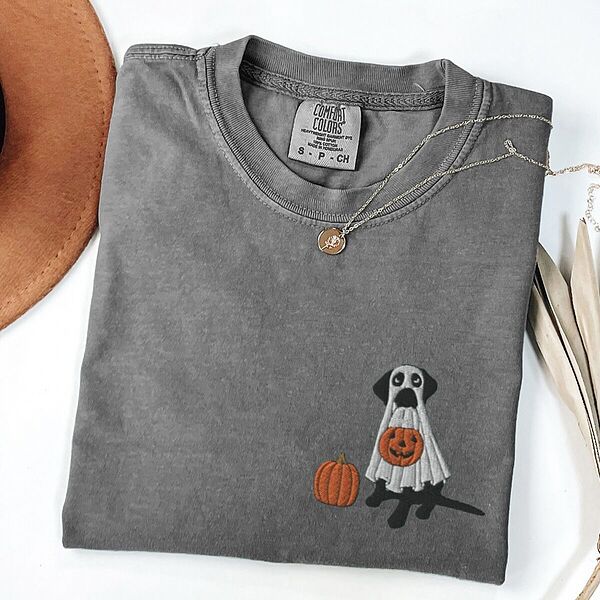 Pepper T-shirt laid flat with a necklace, embroidered with a black lab in a ghost costume and an orange pumpkin