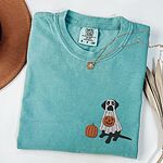 Seafoam T-shirt laid flat with a necklace, embroidered with a black Labrador in a white ghost costume beside a pumpkin
