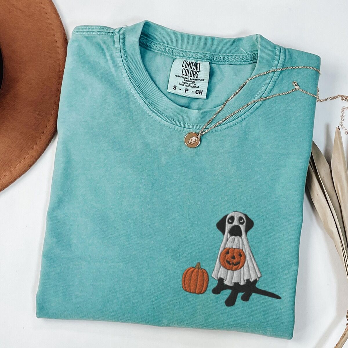 Black Lab Ghost Shirt – Seafoam Seafoam T-shirt laid flat with a necklace, embroidered with a black Labrador in a white ghost costume beside a pumpkin