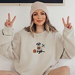 Woman in a knit beanie making peace signs in a Sand crewneck sweatshirt embroidered with a black lab in a ghost sheet, a pumpkin and bats