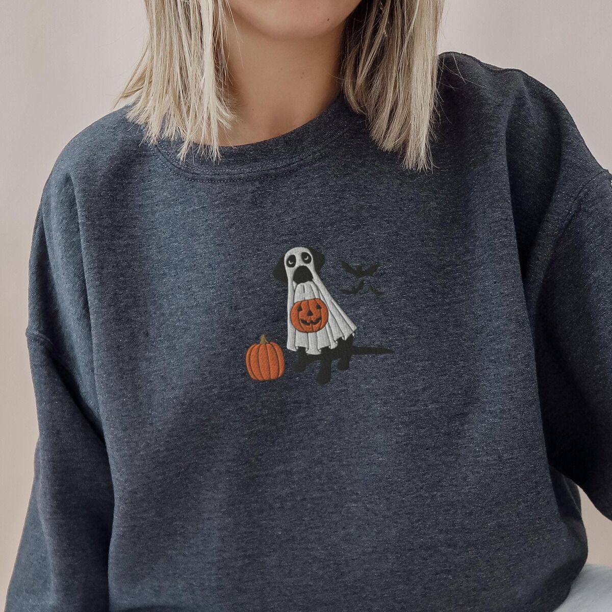 Black Lab Ghost Sweatshirt – Dark Heather Woman in a Dark Heather crewneck sweatshirt embroidered with a black lab under a white ghost sheet with a jack-o'-lantern bucket