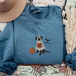 Indigo Blue crewneck sweatshirt laid flat with a felt hat and dried pampas grass, embroidered with a black Labrador trick-or-treating in a ghost sheet