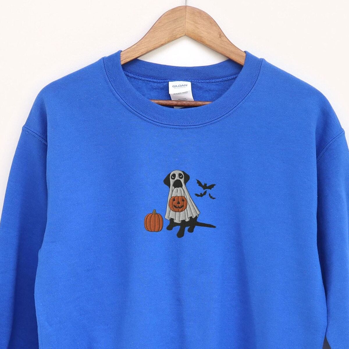 Black Lab Ghost Sweatshirt - Royal Royal crewneck sweatshirt on a wooden hanger, embroidered with a black lab in a white ghost costume, a pumpkin and bats