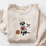 Black lab ghost sweatshirt in Sand laid flat on a white background, embroidered with a black Labrador in a white ghost sheet holding a jack-o'-lantern bucket beside a pumpkin and three bats