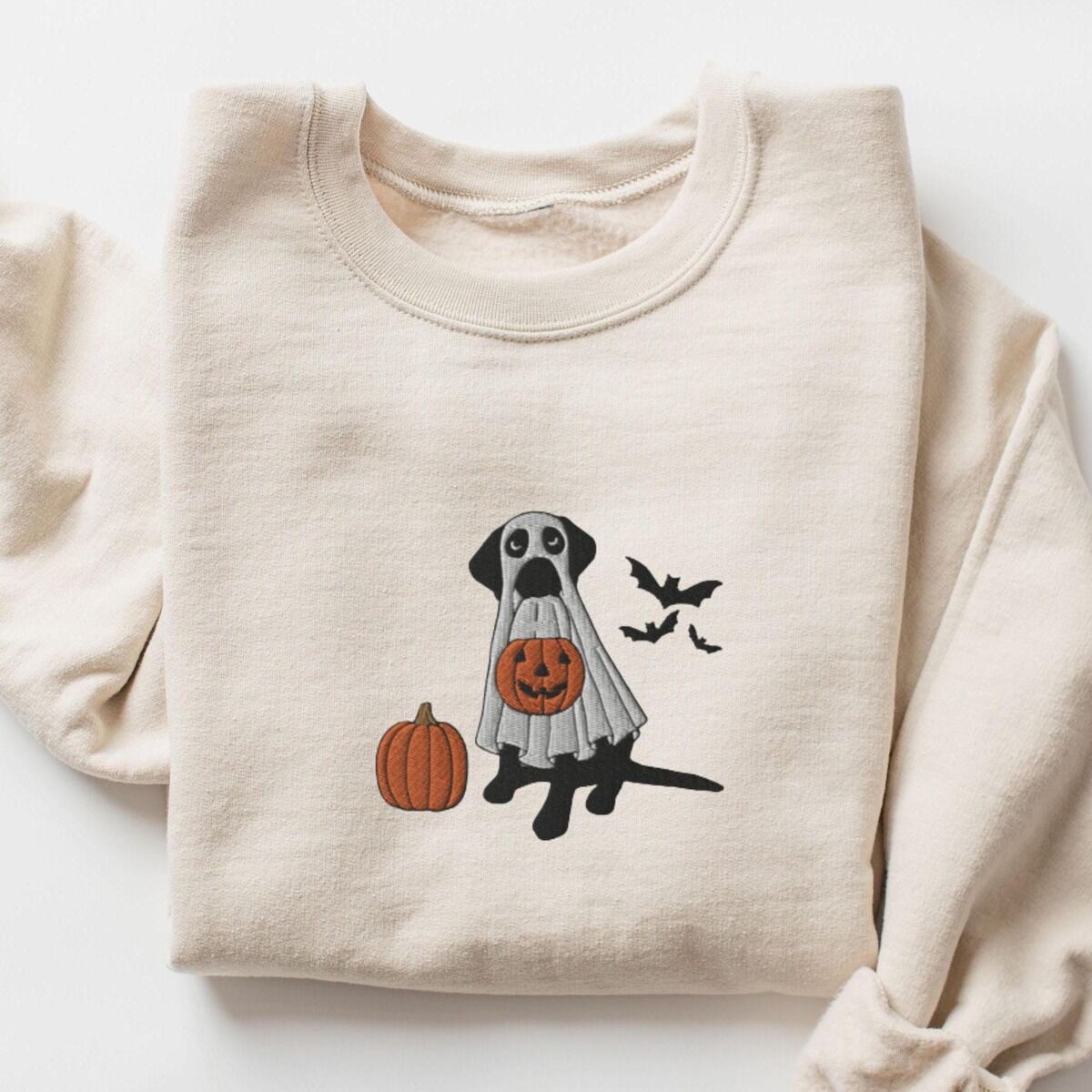 Black Lab Ghost Sweatshirt – Sand Black lab ghost sweatshirt in Sand laid flat on a white background, embroidered with a black Labrador in a white ghost sheet holding a jack-o'-lantern bucket beside a pumpkin and three bats