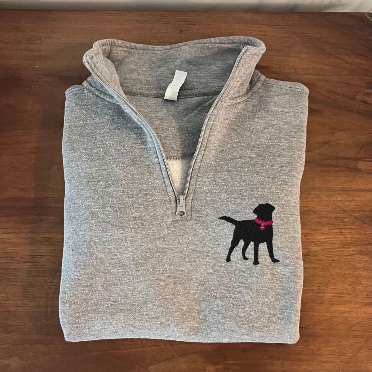 Black Lab Quarter Zip Folded Sport Grey quarter zip pullover on a wooden table with a black Labrador silhouette and a hot pink collar embroidered on the left chest