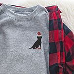 Sport Grey crewneck sweatshirt laid on a buffalo plaid shirt, embroidered with a small black Labrador in a Santa hat and red booties on the left chest