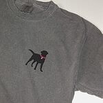 Close-up of the embroidered black Labrador silhouette with a hot pink collar and tag on a dark grey T-shirt