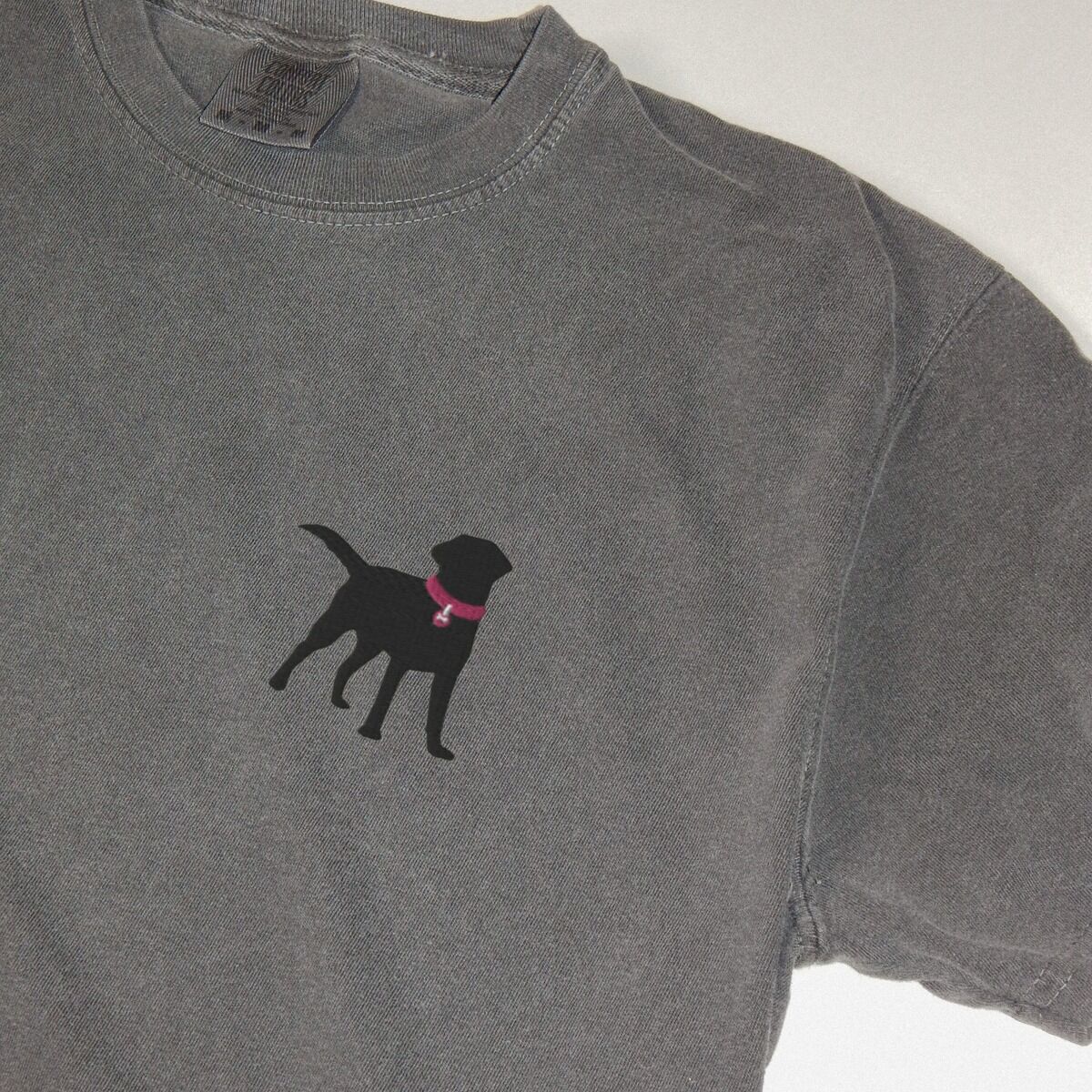 Black Lab Silhouette Shirt - close-up Close-up of the embroidered black Labrador silhouette with a hot pink collar and tag on a dark grey T-shirt