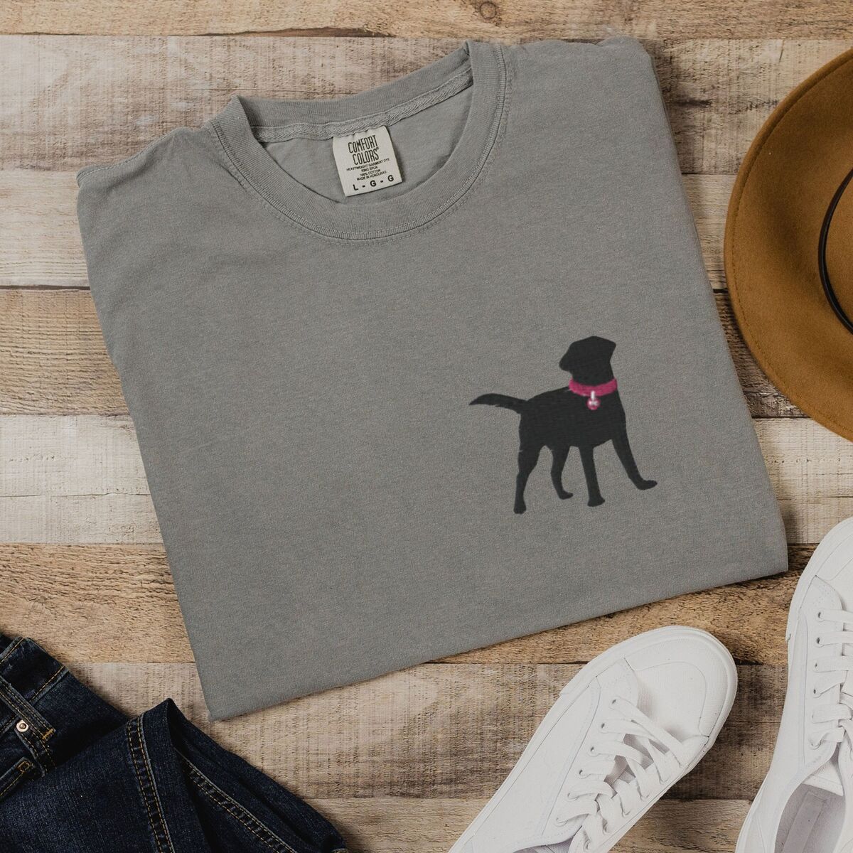 Black Lab Silhouette Shirt - Grey Grey T-shirt laid flat on wood beside jeans and white sneakers, embroidered with a small black Labrador silhouette in a hot pink collar and tag on the left chest