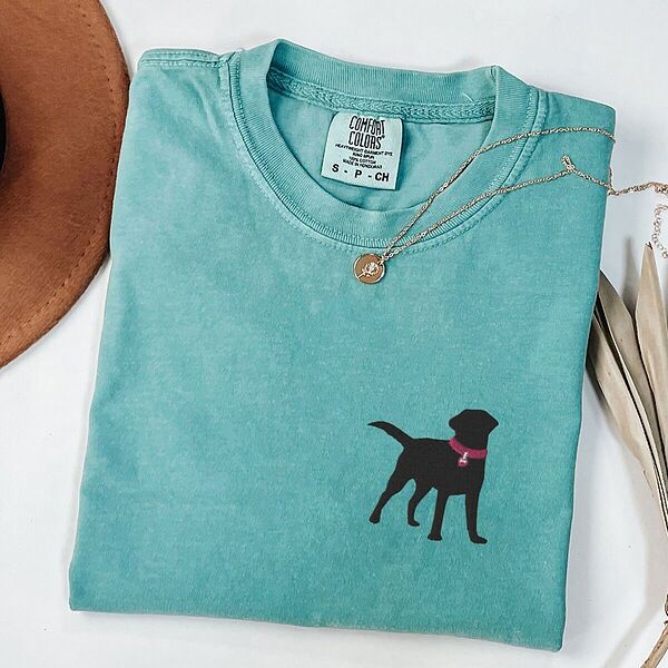 Seafoam T-shirt laid flat with a necklace, embroidered with a small black Labrador silhouette in a hot pink collar and tag on the left chest