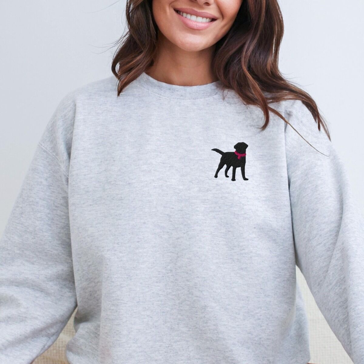 Black Lab Silhouette Sweatshirt – Ash Smiling woman in an Ash crewneck sweatshirt embroidered with a small black Labrador silhouette in a hot pink collar on the left chest