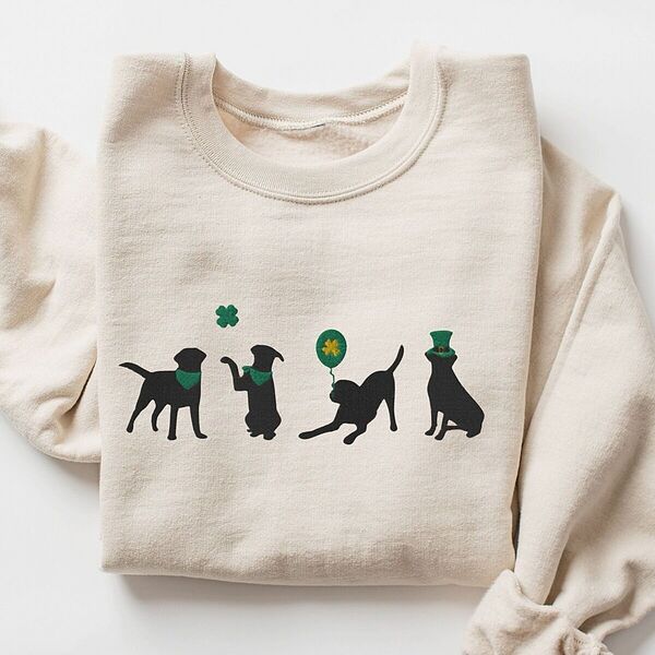 Sand crewneck sweatshirt laid flat, embroidered with four black lab silhouettes in green bandanas with a shamrock, a clover balloon and a leprechaun hat