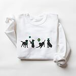 White crewneck sweatshirt laid flat, embroidered with four black lab silhouettes in green bandanas with a shamrock, a clover balloon and a leprechaun hat