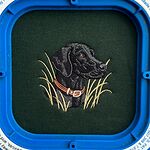 Forest Green sweatshirt held in a blue magnetic embroidery hoop with a freshly stitched black Labrador head in a rust leather collar among tall pale marsh grass