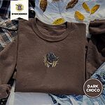 Dark Chocolate crewneck sweatshirt on a plaid flannel shirt with yellow autumn leaves and denim shorts, embroidered with a black Labrador head with a rust leather collar in tall marsh grass