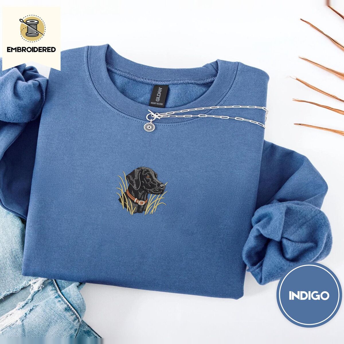 Black Lab Sweatshirt – Indigo Blue Indigo Blue crewneck sweatshirt folded with light jeans and dried twigs, embroidered with a black Labrador head with a rust leather collar in tall marsh grass