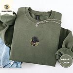 Military Green crewneck sweatshirt folded with light jeans and a silver chain necklace, embroidered with a black Labrador head with a rust leather collar in tall marsh grass
