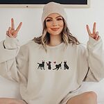 Woman in a beanie making peace signs in a Sand crewneck sweatshirt embroidered with four black lab silhouettes in red heart headbands with a red bandana and a heart balloon