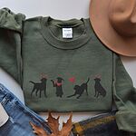 Military Green crewneck sweatshirt laid flat with a felt hat and jeans, embroidered with four black lab silhouettes in red heart headbands with a red bandana and a heart balloon