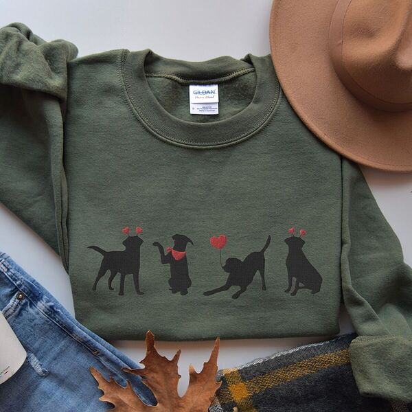 Military Green crewneck sweatshirt laid flat with a felt hat and jeans, embroidered with four black lab silhouettes in red heart headbands with a red bandana and a heart balloon