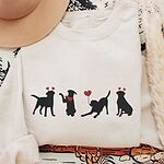 Sand crewneck sweatshirt laid flat with a tan hat and dried pampas, embroidered with four black lab silhouettes in red heart headbands with a red bandana and a heart balloon