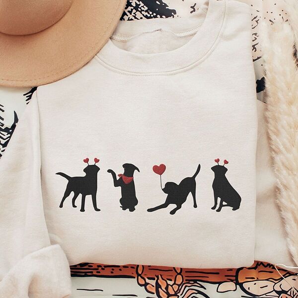 Sand crewneck sweatshirt laid flat with a tan hat and dried pampas, embroidered with four black lab silhouettes in red heart headbands with a red bandana and a heart balloon