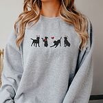 Smiling woman in a Sport Grey crewneck sweatshirt embroidered with four black lab silhouettes in red heart headbands with a red bandana and a heart balloon