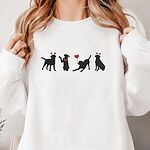 Smiling woman in a White crewneck sweatshirt embroidered with four black lab silhouettes in red heart headbands with a red bandana and a heart balloon