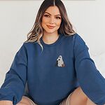 Smiling woman sitting in a blue crewneck sweatshirt embroidered with a small ghost lab mom sipping red wine with a black lab sitting against her and a jack-o'-lantern, on the left chest