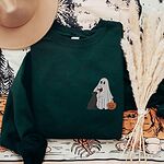 Forest Green crewneck sweatshirt laid flat with a brown hat and pampas grass, embroidered with a small ghost lab mom sipping red wine with a black lab sitting against her and a jack-o'-lantern, on the left chest