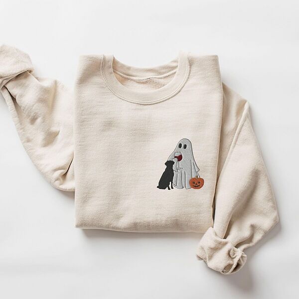 Sand crewneck sweatshirt laid flat on a white background, embroidered with a small ghost lab mom sipping red wine with a black lab sitting against her and a jack-o'-lantern, on the left chest