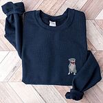 Navy crewneck sweatshirt laid flat on a wood floor, embroidered with a small blue-grey pit bull sitting with its pink tongue out on the left chest