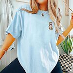 Woman in a Chambray T-shirt embroidered with a small fawn and white pit bull sitting with its pink tongue out on the left chest