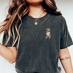 Woman in a Pepper T-shirt embroidered with a small fawn and white pit bull sitting with its pink tongue out on the left chest
