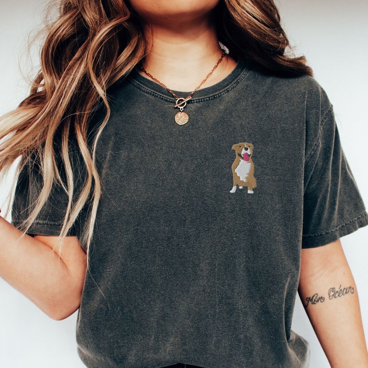 Brown and White Pitbull Shirt – Pepper Woman in a Pepper T-shirt embroidered with a small fawn and white pit bull sitting with its pink tongue out on the left chest