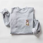 Sport Grey crewneck sweatshirt laid flat with a rolled cuff, embroidered with a small fawn and white pit bull sitting with its pink tongue out on the left chest