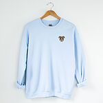 Light Blue crewneck sweatshirt on a hanger, embroidered with a small minimalist fawn and white pit bull face with grey ears on the left chest