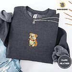 Dark Heather crewneck sweatshirt folded with ripped jeans and a silver chain necklace, embroidered with a fawn and cream English bulldog puppy in a red collar chewing a string of Christmas lights