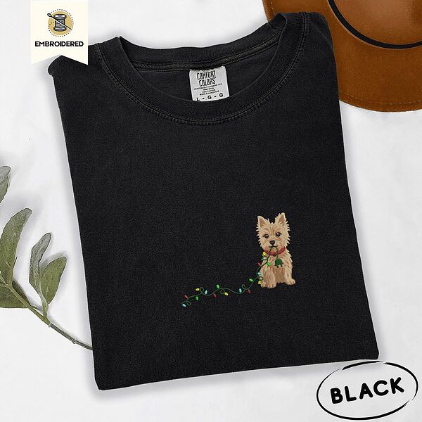 Black Comfort Colors T-shirt embroidered with a wheaten Cairn terrier puppy in a red collar chewing the plug of a string of Christmas lights