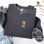 Dark Heather crewneck sweatshirt folded with ripped jeans and a silver chain necklace, embroidered with a wheaten Cairn terrier puppy in a red collar chewing the plug of a string of Christmas lights