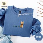 Indigo Blue crewneck sweatshirt folded with light jeans and dried twigs, embroidered with a wheaten Cairn terrier puppy in a red collar chewing the plug of a string of Christmas lights