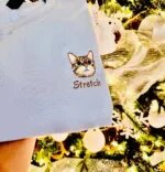 Light blue sweatshirt with an embroidered tabby cat face and the name Stretch on the chest