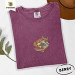 Berry Comfort Colors T-shirt embroidered with an orange tabby cat asleep on a stack of green, brown and rust red books